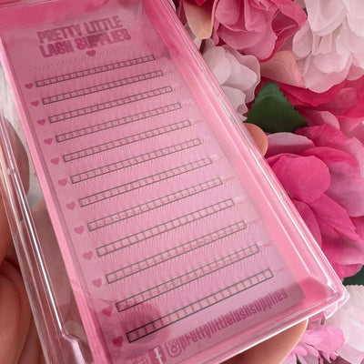 Pink lash extension tray featuring various lengths of soft, synthetic lashes in a heart-patterned packaging.