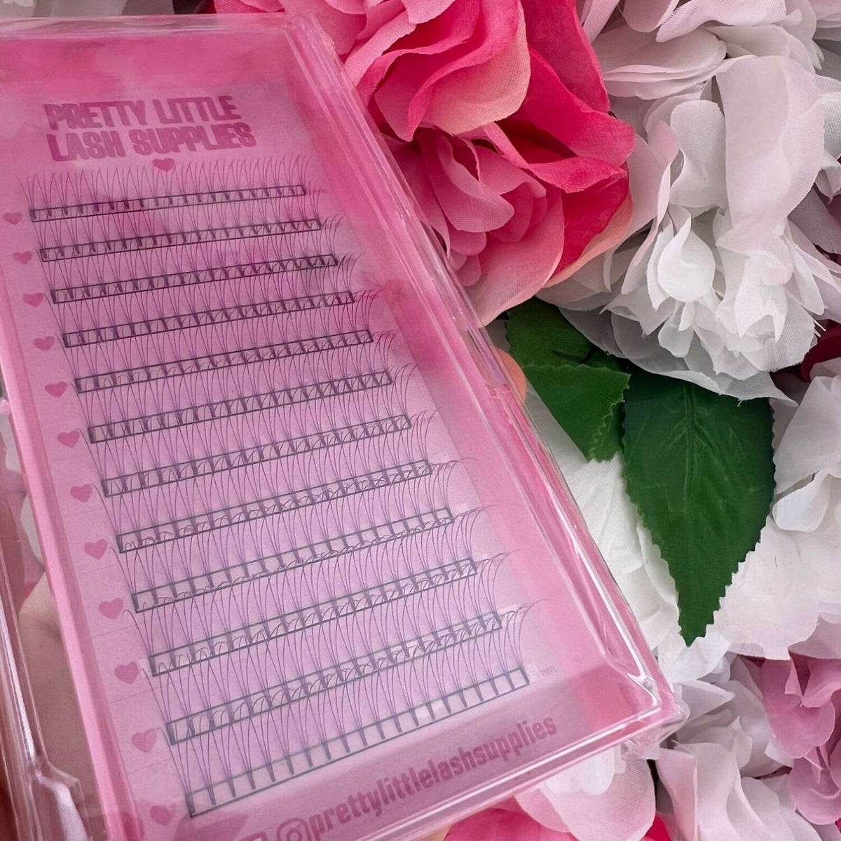 Pretty Little Lash Supplies pink eyelash extension tray with various lengths, surrounded by soft floral petals.