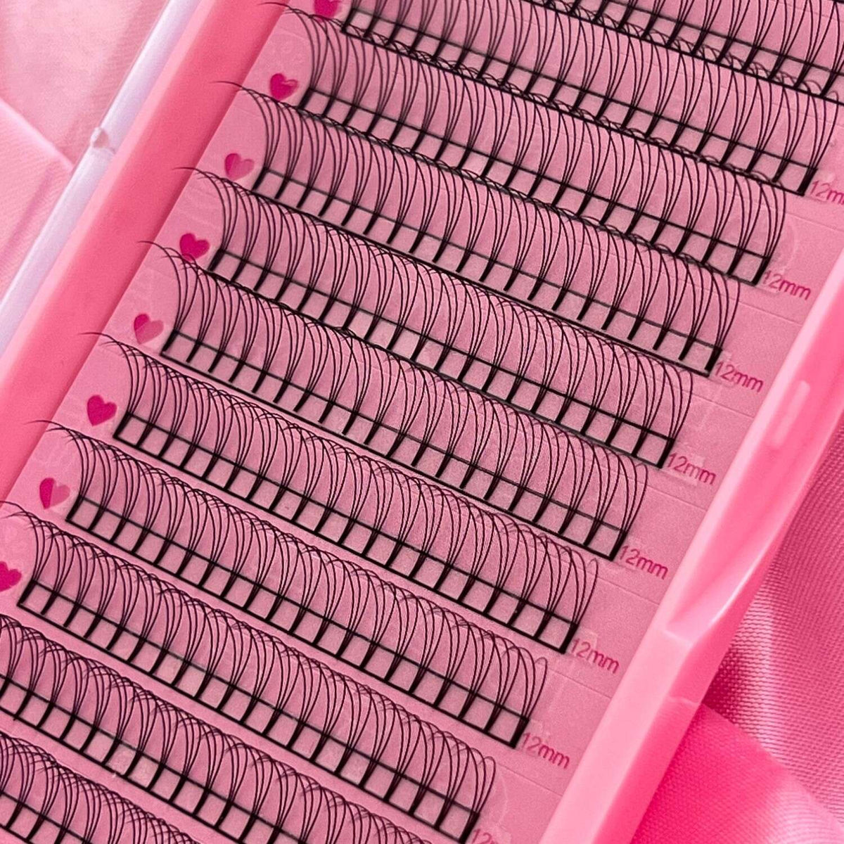 Pink eyelash extension tray, featuring 12mm black lashes with heart-patterned adhesive strips, ideal for volumizing.