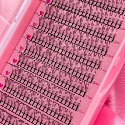 Pink eyelash extension tray, featuring 12mm black lashes with heart-patterned adhesive strips, ideal for volumizing.