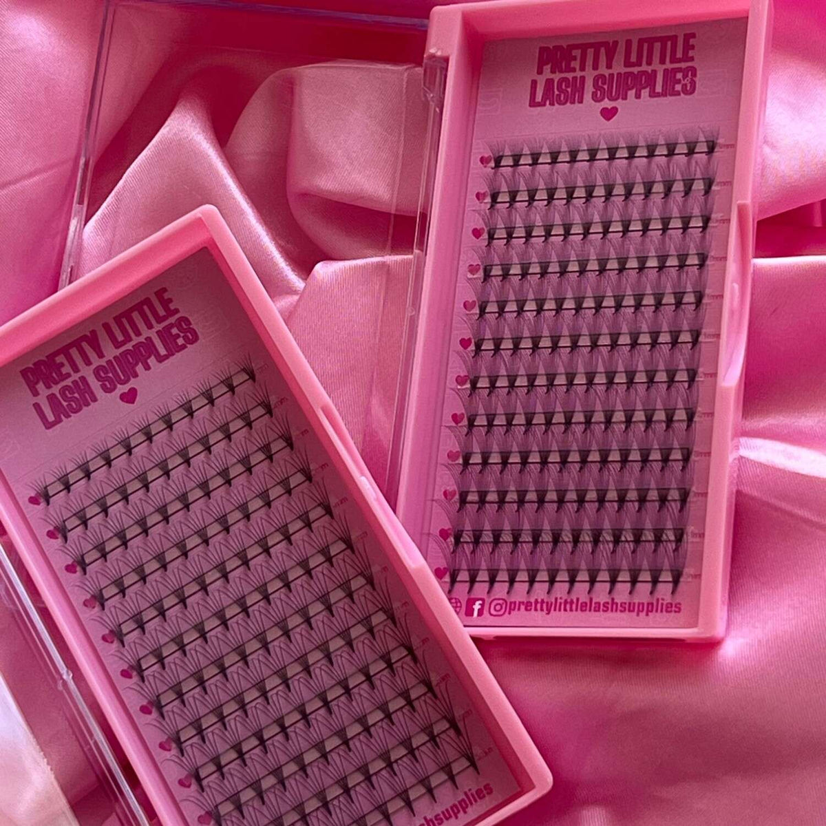 Pink eyelash extension trays with black lashes, showcasing various lengths and styles, inside a glossy pink case.