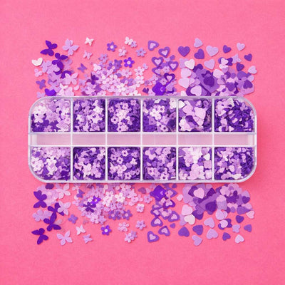 Purple glitter sequins in assorted shapes, including hearts and flowers, in a clear storage box on a pink background.