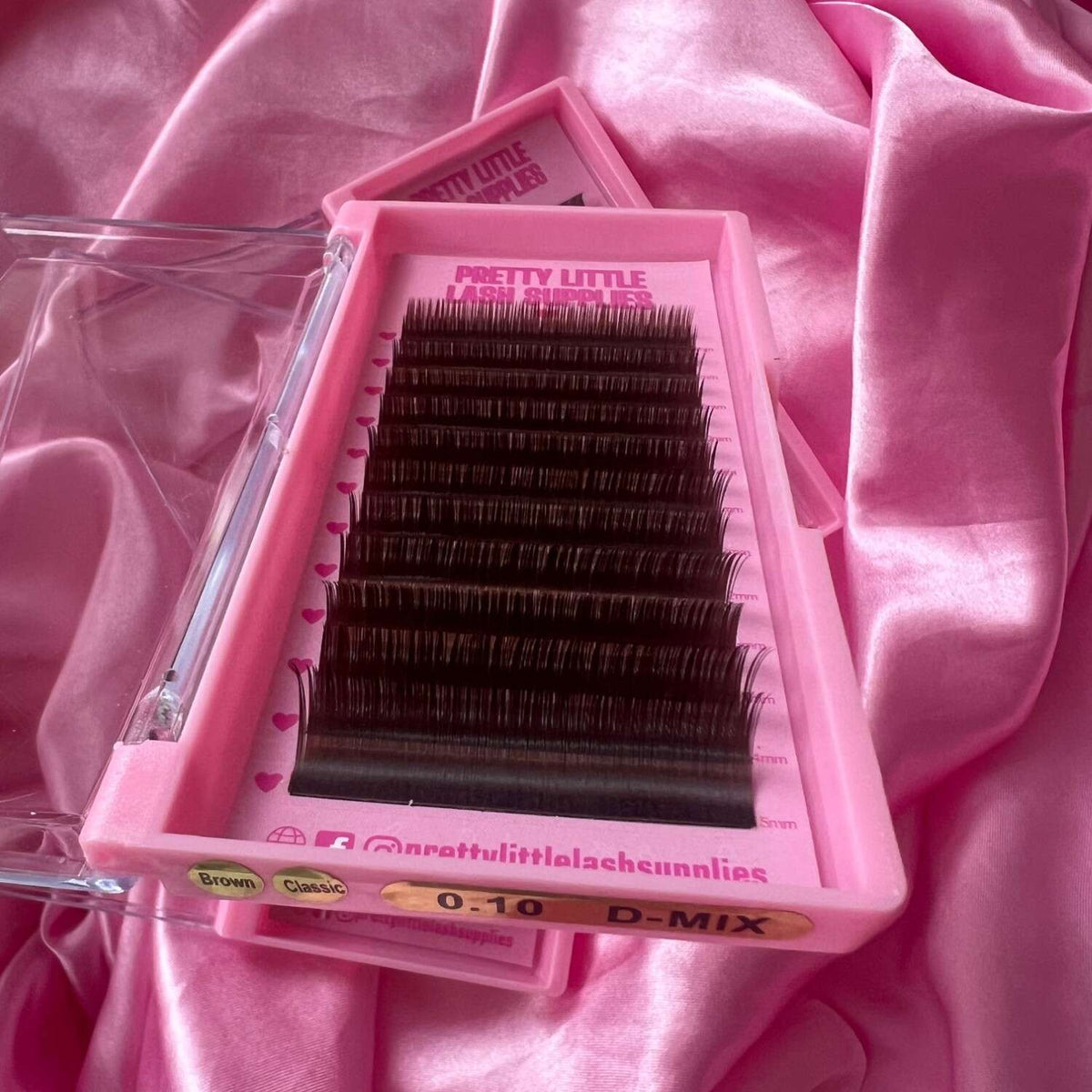 D-Mix eyelash extensions in classic black, 0.10 thickness, neatly arranged in a pink tray on silky pink fabric.