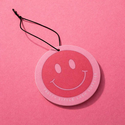 Pink circular car scent with a smiley face, featuring "Pretty Little Lash Supplies" in white text. Stylish, fun design.