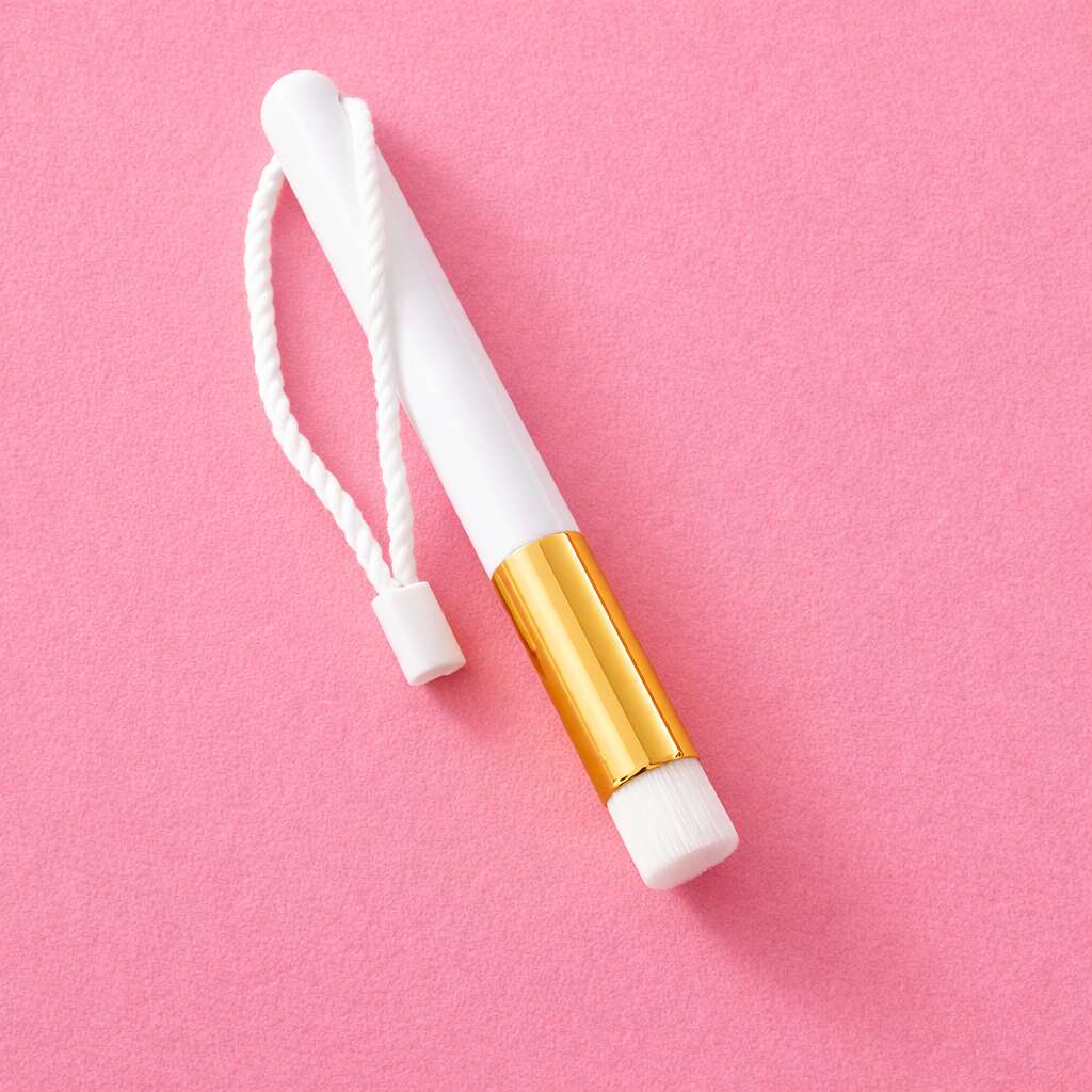 White makeup brush with gold accents and a braided rope on a pink background. Ideal for precision application.