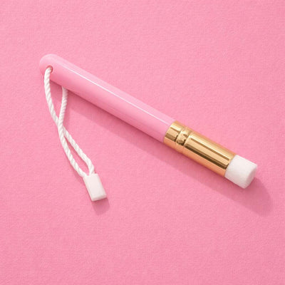 Pink makeup brush with a soft white tip and a gold accent, featuring a convenient white strap for easy handling.