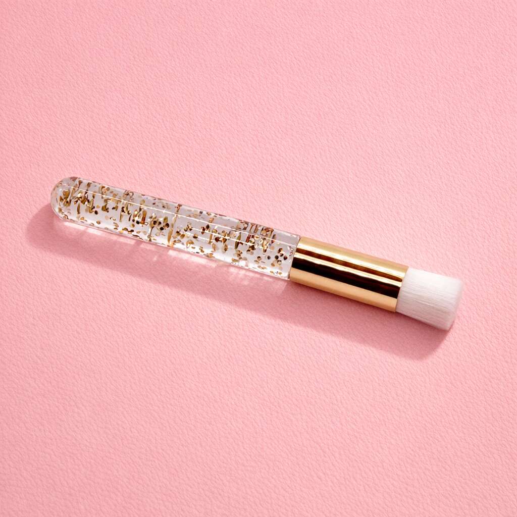 Clear cosmetic brush with gold glitter, white bristles, and a chic gold handle over a soft pink background.