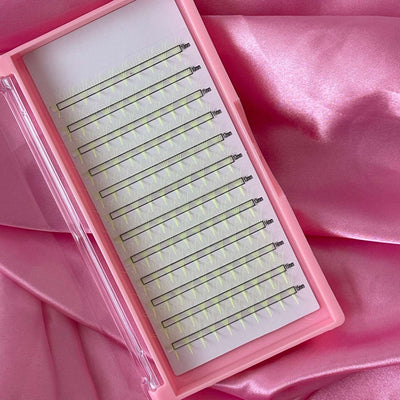 Pink eyelash extension tray with clear plastic case, featuring multiple rows of green lash strips. Perfect for volumizing.