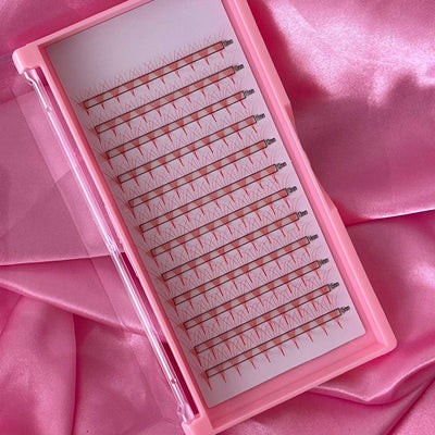 Pink eyelash extension tray with mixed-length, tapered, red lashes on a glossy white sheet. Perfect for volume sets.