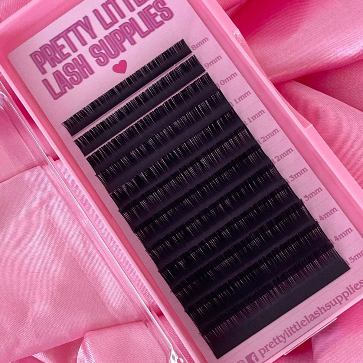 Black eyelash extension strips in varying lengths on a pink background from Pretty Little Lash Supplies.