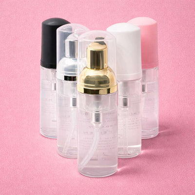 Clear spray bottles with gold, silver, black, pink, and white caps, ideal for travel or skincare.