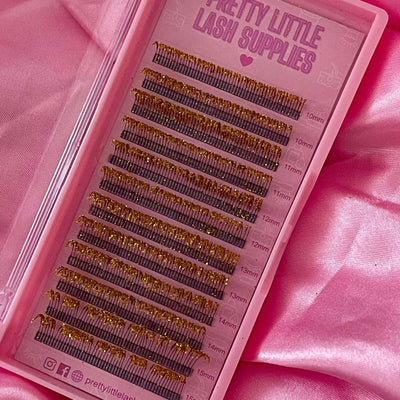 Gold glitter eyelash extensions in varying lengths (10-15mm) on a pink tray, perfect for enhancing lash looks.