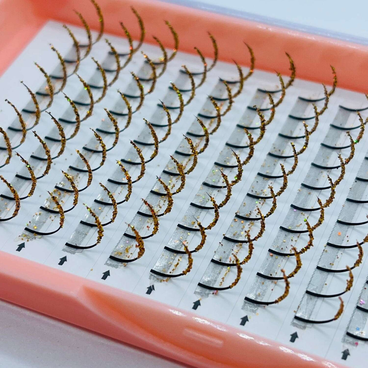 Brown glitter eyelash extensions in a pink tray, offering volume and drama for a glamorous look.