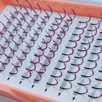 Pink glitter eyelash extensions with black bases in a clear tray, perfect for glam makeup looks.