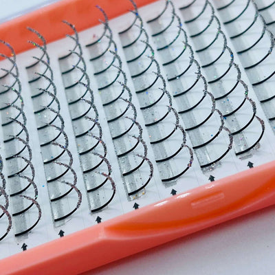 Silver glitter eyelash extensions on a white tray, featuring a curly style with a soft pink plastic packaging.