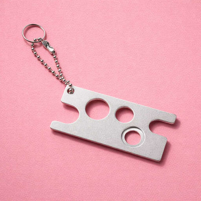 Silver keychain multitool with three holes, crafted from sturdy metal, against a pink background.