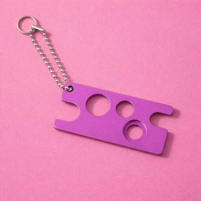 Purple aluminum keychain with multiple holes and a silver ball chain on a pink background.