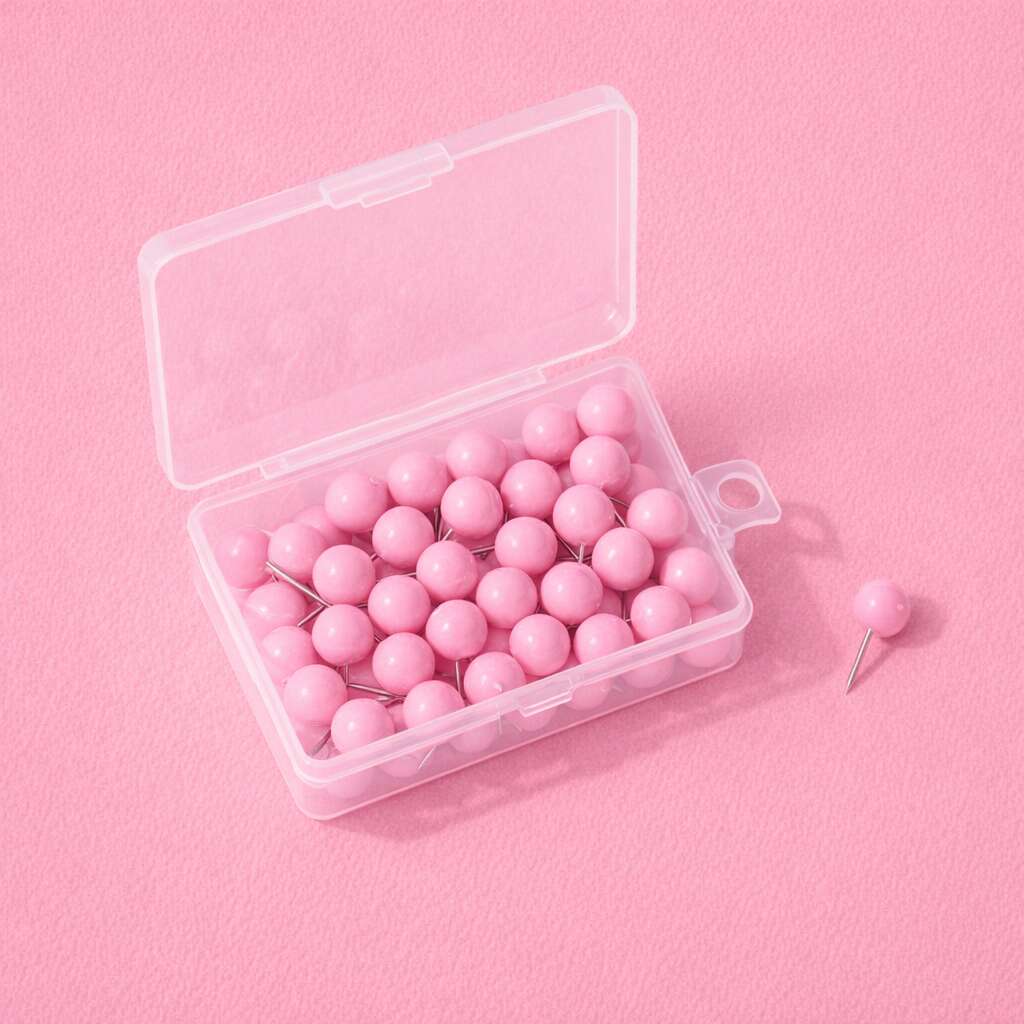 Pink push pins in a clear plastic box on a soft pink background. Ideal for organization and crafting.