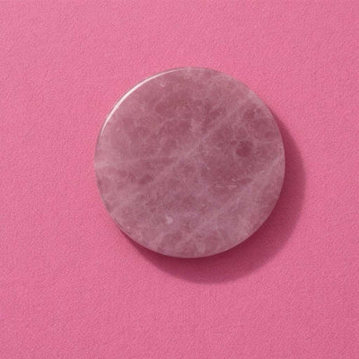 Round pink rose quartz facial roller stone on a vibrant pink background for skincare and beauty routines.