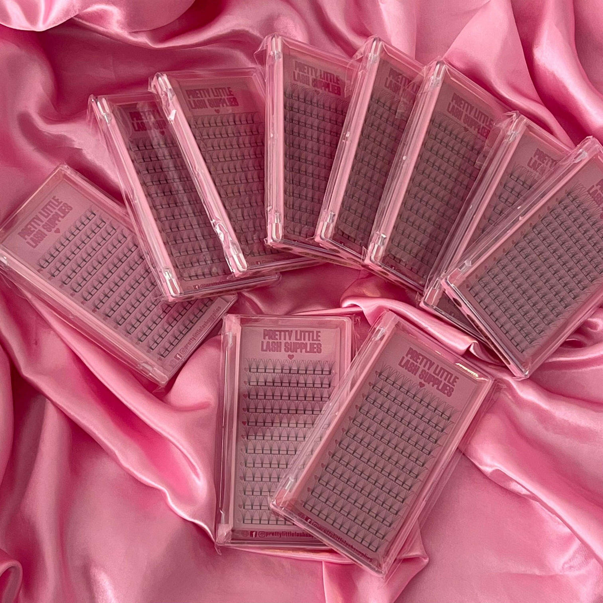Multiple trays of 'Pretty Little Lash Supplies' lash extensions on a pink satin background