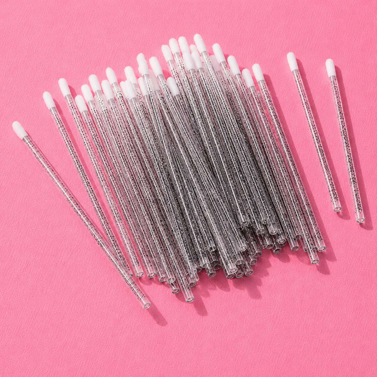 Clear plastic cotton swabs with white tips, perfect for beauty and personal care, neatly arranged on a pink background.