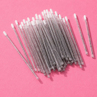 Clear plastic cotton swabs with white tips, perfect for beauty and personal care, neatly arranged on a pink background.