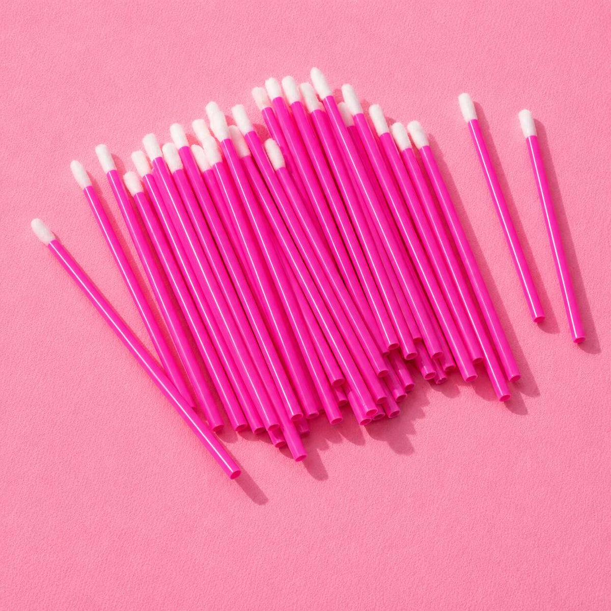 Bright pink cotton swabs with plastic sticks, perfect for makeup application and touch-ups on a vibrant pink background.