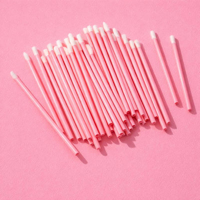 Pink cosmetic applicators with white tips, ideal for makeup application and touch-ups, neatly arranged on a pastel pink background.