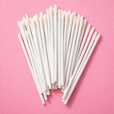 White disposable foam applicators on a pink background, perfect for makeup and beauty applications.