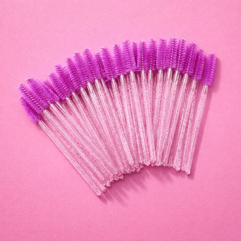 Purple mascaras wands with clear handles, perfect for eyelash and eyebrow grooming, set against a pink background.
