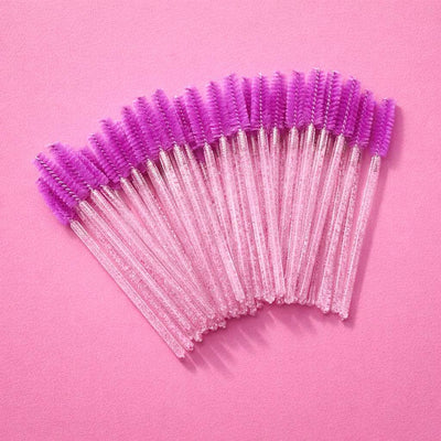 Purple mascaras wands with clear handles, perfect for eyelash and eyebrow grooming, set against a pink background.