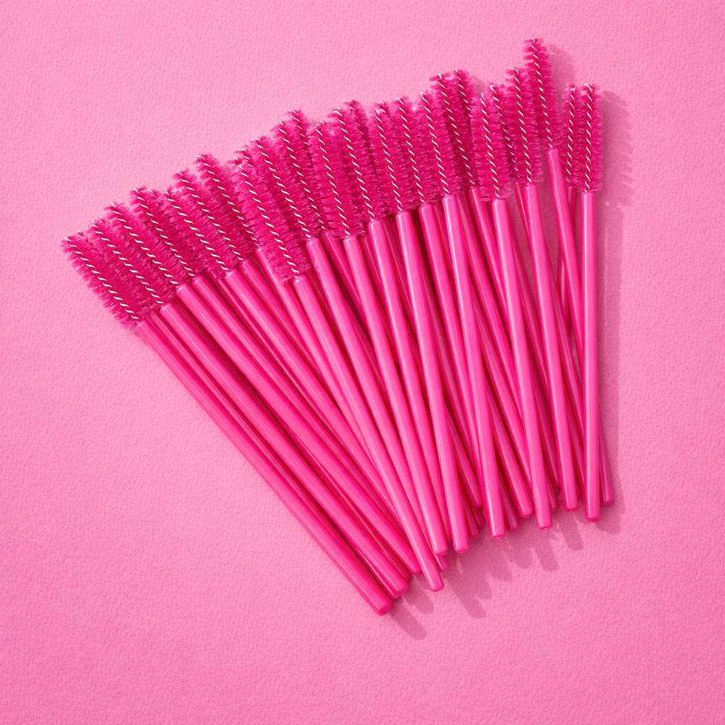 Pink disposable mascara wands with spiral bristles arranged on a vibrant pink backdrop.