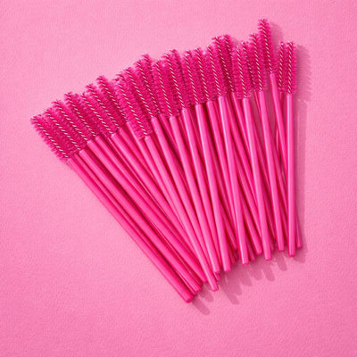 Pink disposable mascara wands with spiral bristles arranged on a vibrant pink backdrop.