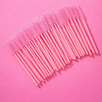 Pack of 25 pink disposable mascara wands with clear plastic handles on a pink background. Perfect for makeup applications.