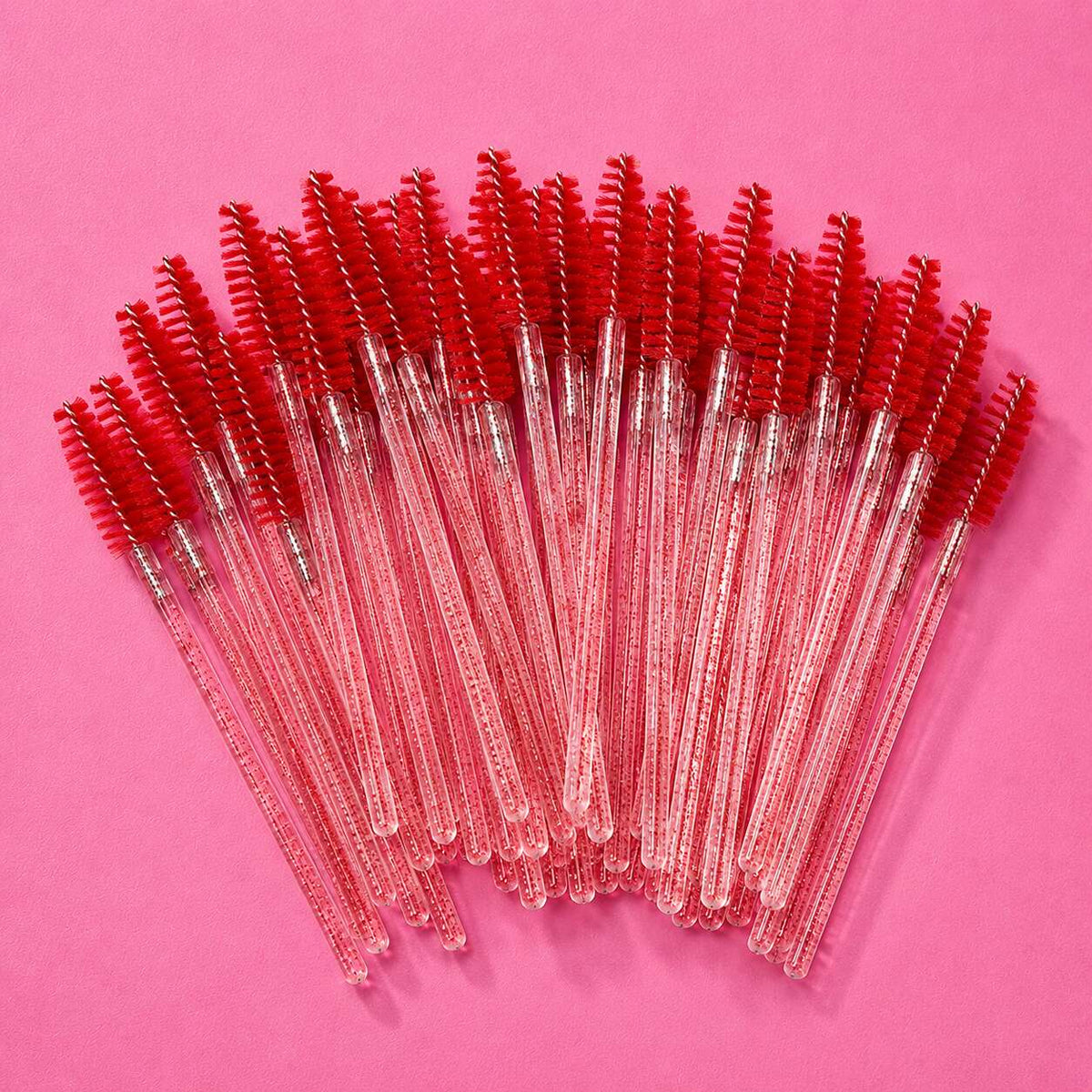 Set of 25 clear handle mascara wands with bright red bristles on a pink background. Perfect for beauty applications.