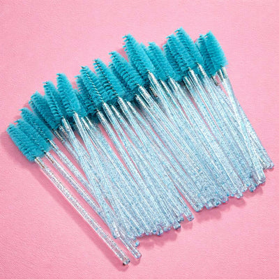 A set of 25 turquoise eyelash brushes with clear glitter handles on a pink background.