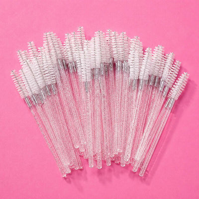 Clear mascara wands with soft pink bristles, perfect for precise application and grooming, set against a vibrant pink background.