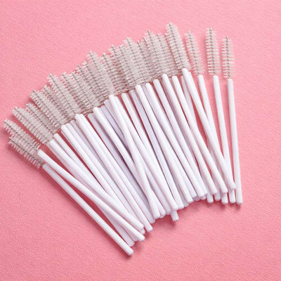 White disposable mascara wands with plastic handles arranged on a pink background. Ideal for beauty professionals.