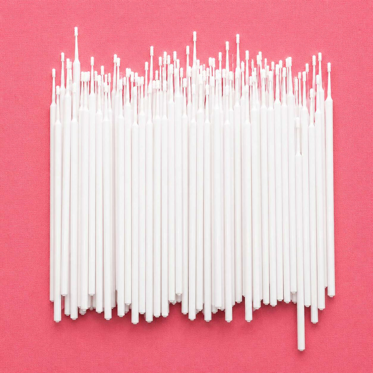 Set of 100 white, thin wax candle wicks on a pink background, perfect for DIY candle making projects.