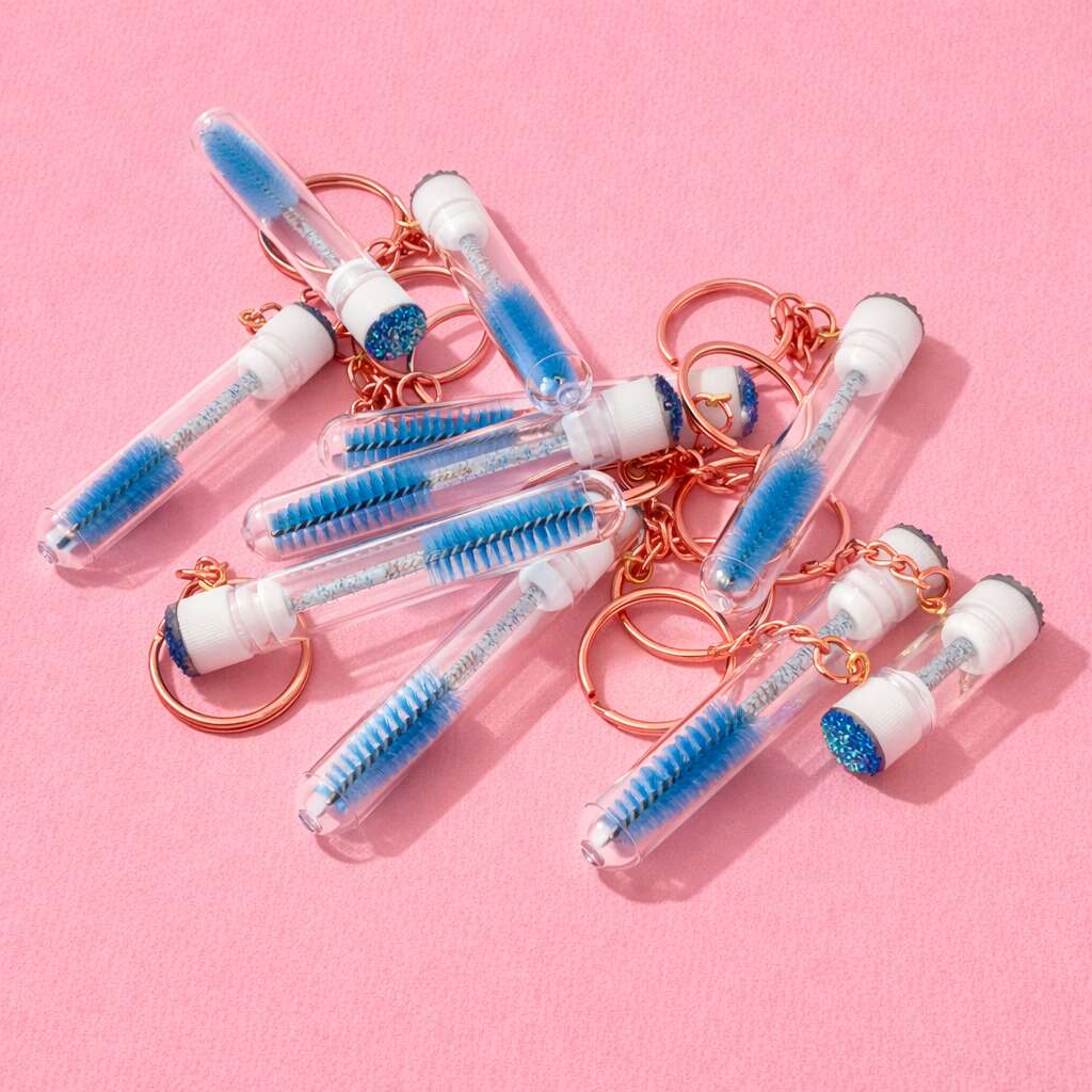 Blue glitter keychain brushes with transparent tubes and rose gold accents on a pink background.