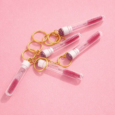 Glamorous pink eyelash brush keychain set in clear tubes with gold accents, perfect for beauty enthusiasts.