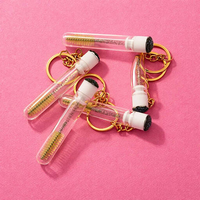 Gold keychain with clear test tubes and screws, featuring a modern, playful design on a pink background.
