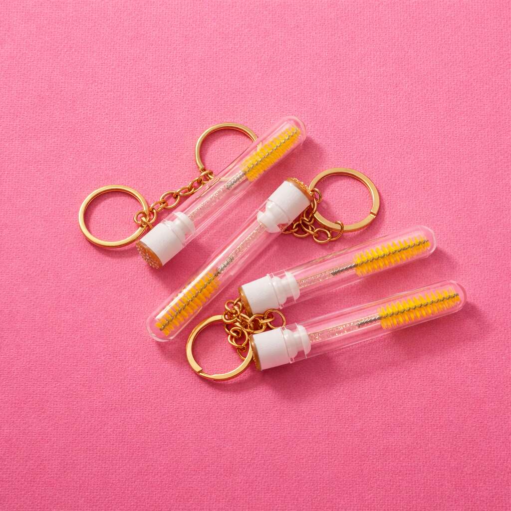 Clear keychain mini toothbrushes with yellow bristles and gold accents on a pink background.