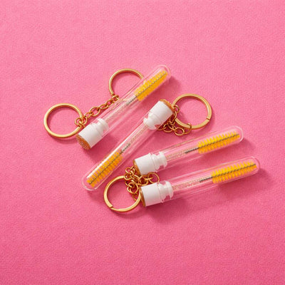 Clear keychain mini toothbrushes with yellow bristles and gold accents on a pink background.