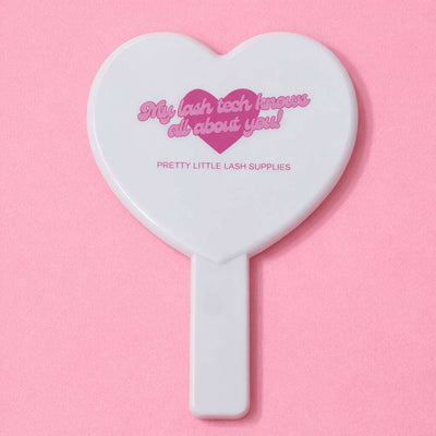 White heart-shaped cosmetic mirror with pink text "My lash tech knows all about you!" from Pretty Little Lash Supplies.