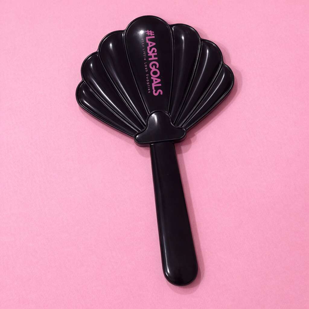 Black shell-shaped cosmetic mirror with "#LashGoals" text on a pink background. Perfect for beauty enthusiasts.