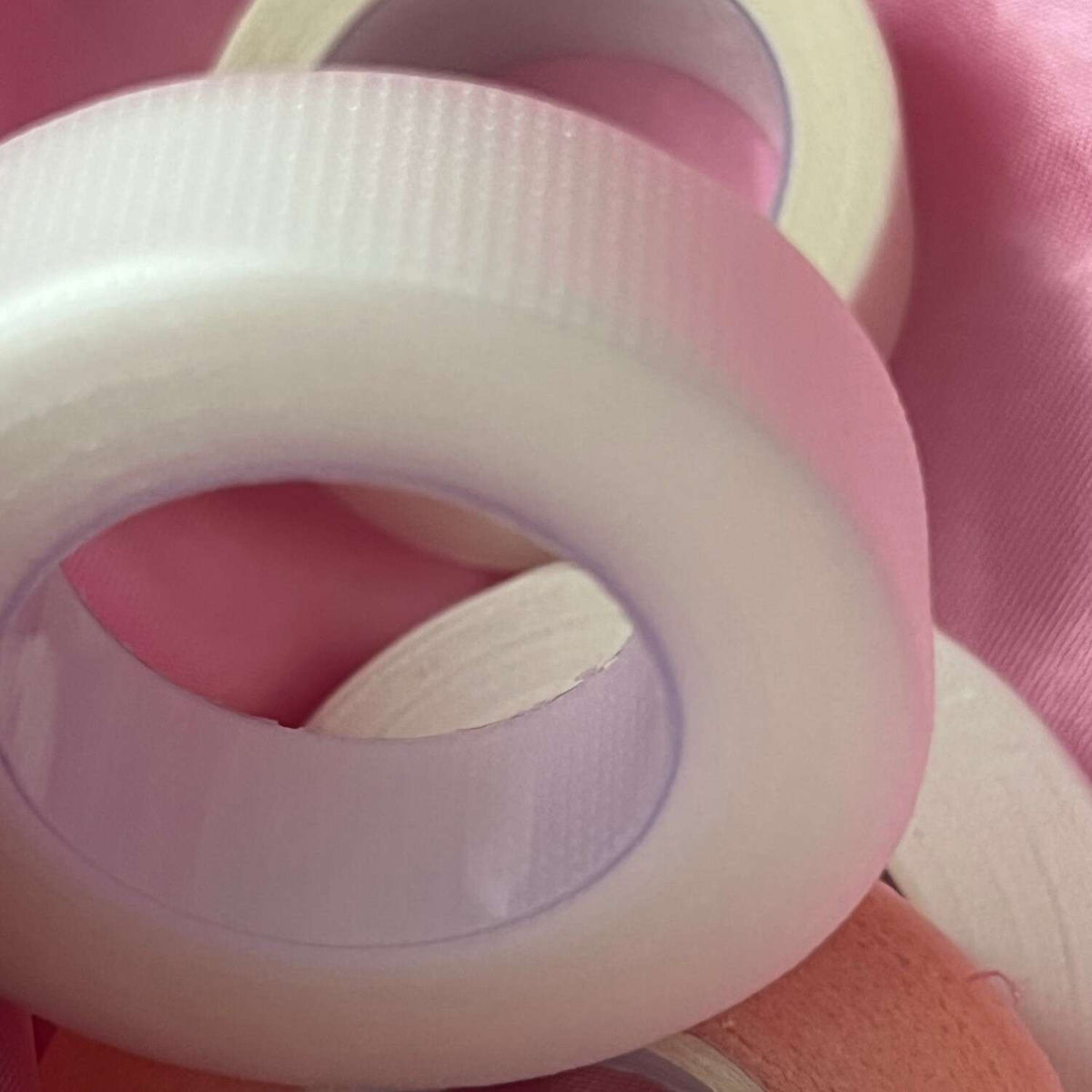 White washi tape rolls on a pink fabric background, textured for crafting and decorating projects.