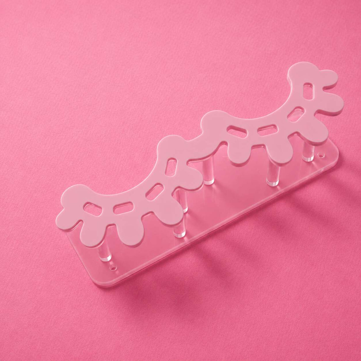 Pink acrylic hair accessory organizer with playful design, featuring six pegs for storage.