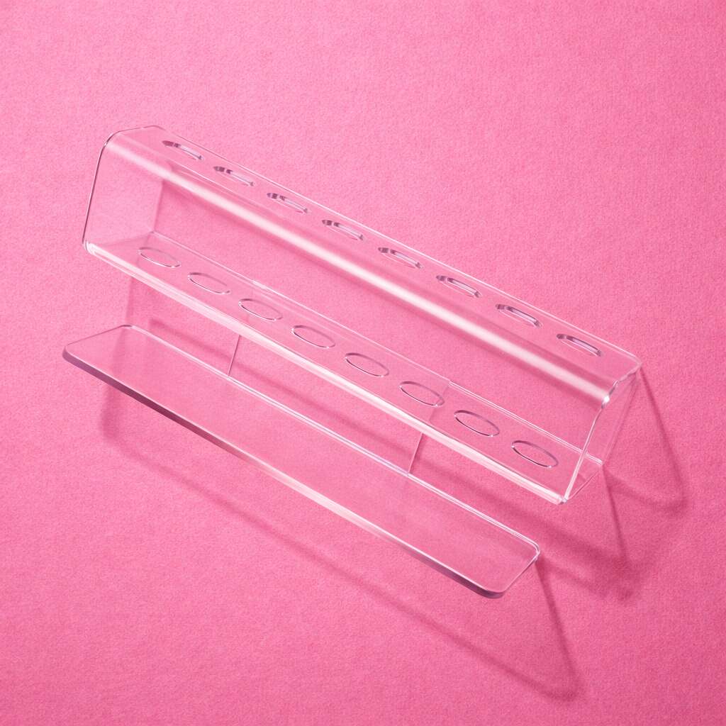 Clear acrylic pen holder with multiple slots, modern design, ideal for office or desk organization against a pink background.