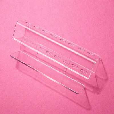 Clear acrylic pen holder with multiple slots, modern design, ideal for office or desk organization against a pink background.